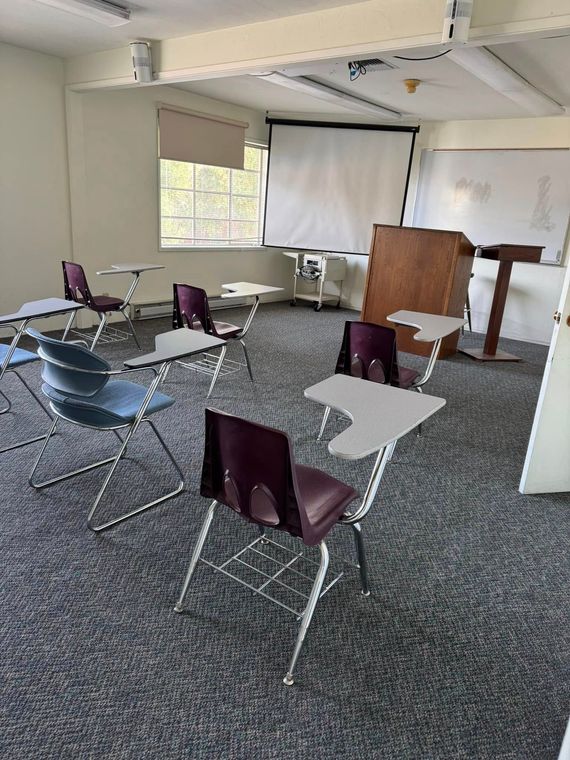 A classroom with desks and chairs and a projector screen.