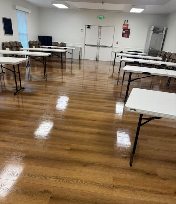 A large room with wooden floors and white tables and chairs.