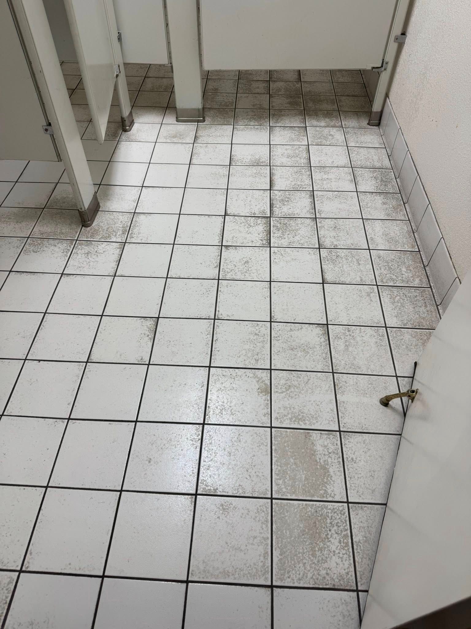 A dirty tiled floor in a bathroom with a door open