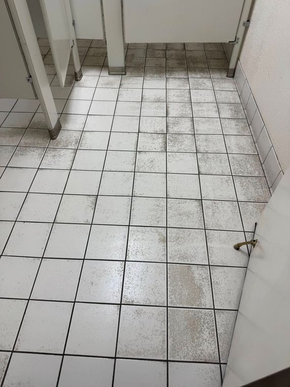 A dirty tiled floor in a bathroom with a door open