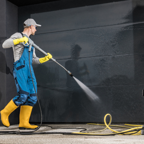 A man is using a high pressure washer to clean a garage door.