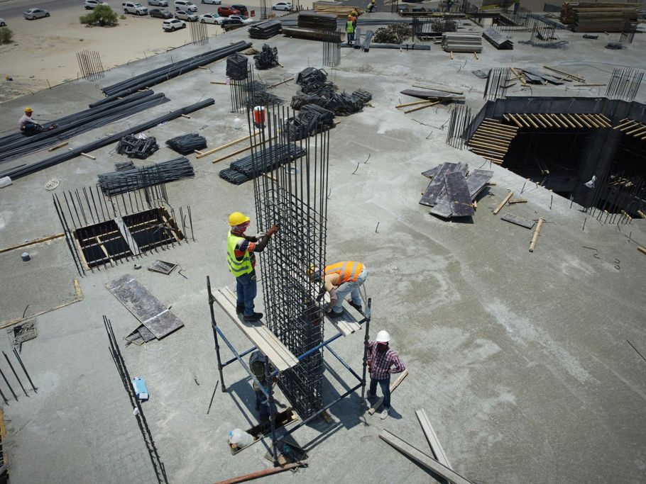Construction workers assembling rebar columns at a building site with concrete forms and excavation nearby