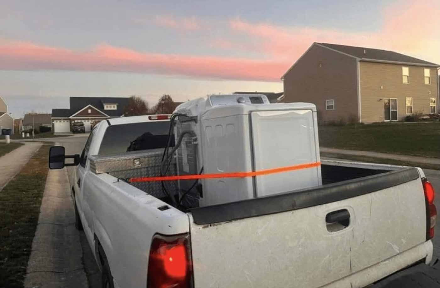 A white truck with a washer and dryer in the back is parked on the side of the road.