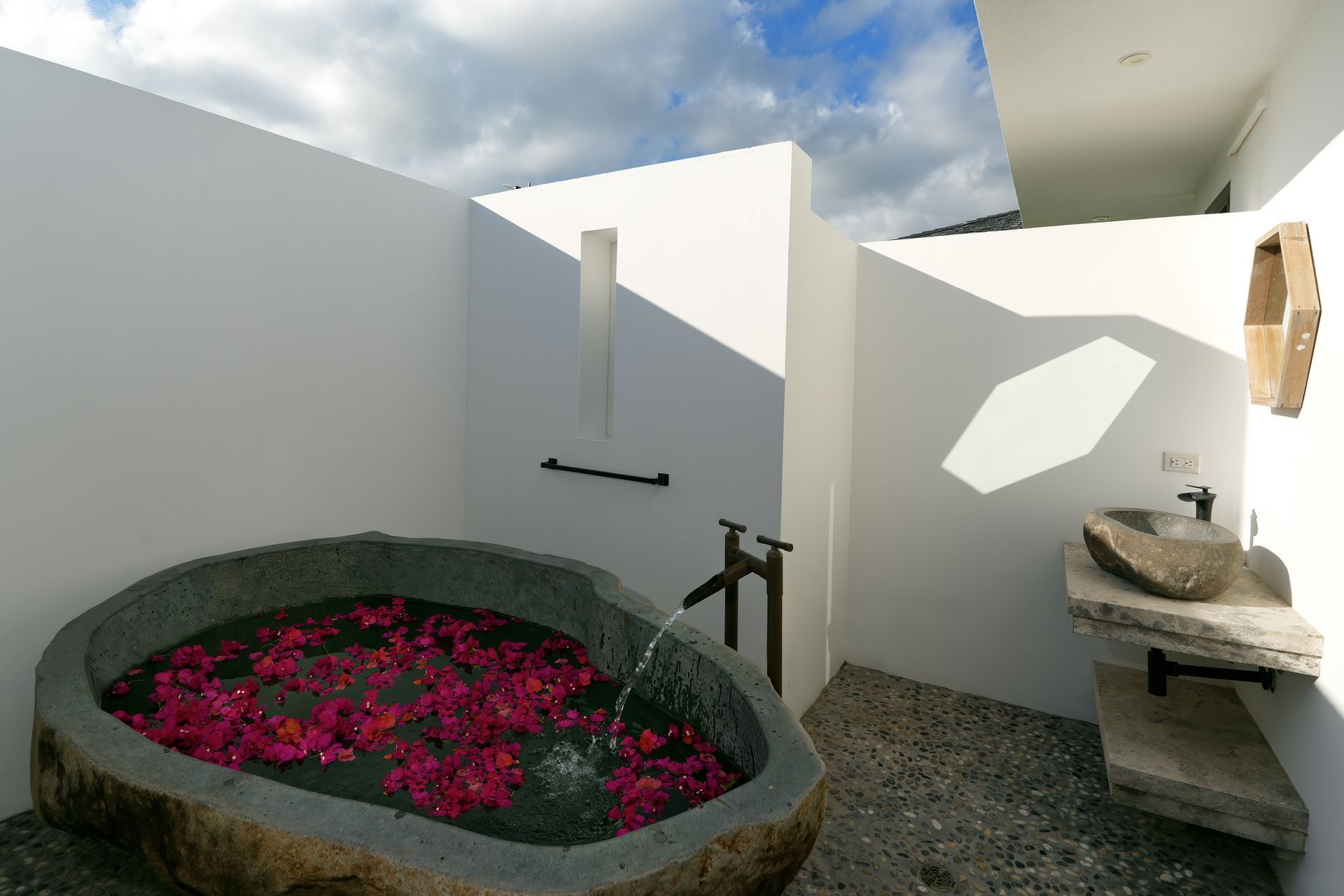 A bathroom with a stone bathtub filled with pink flowers