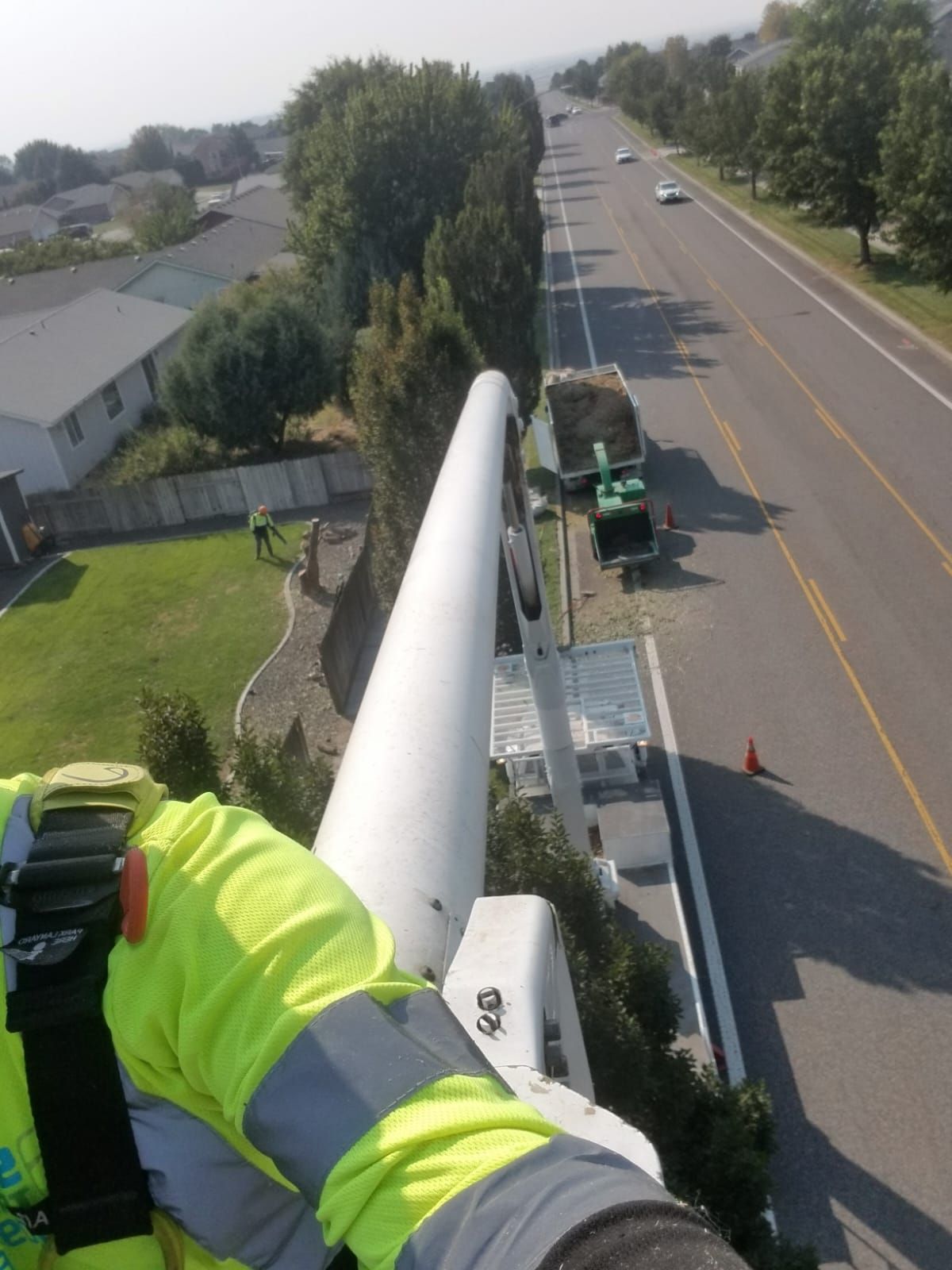 A person in a yellow safety vest is standing on a pole
