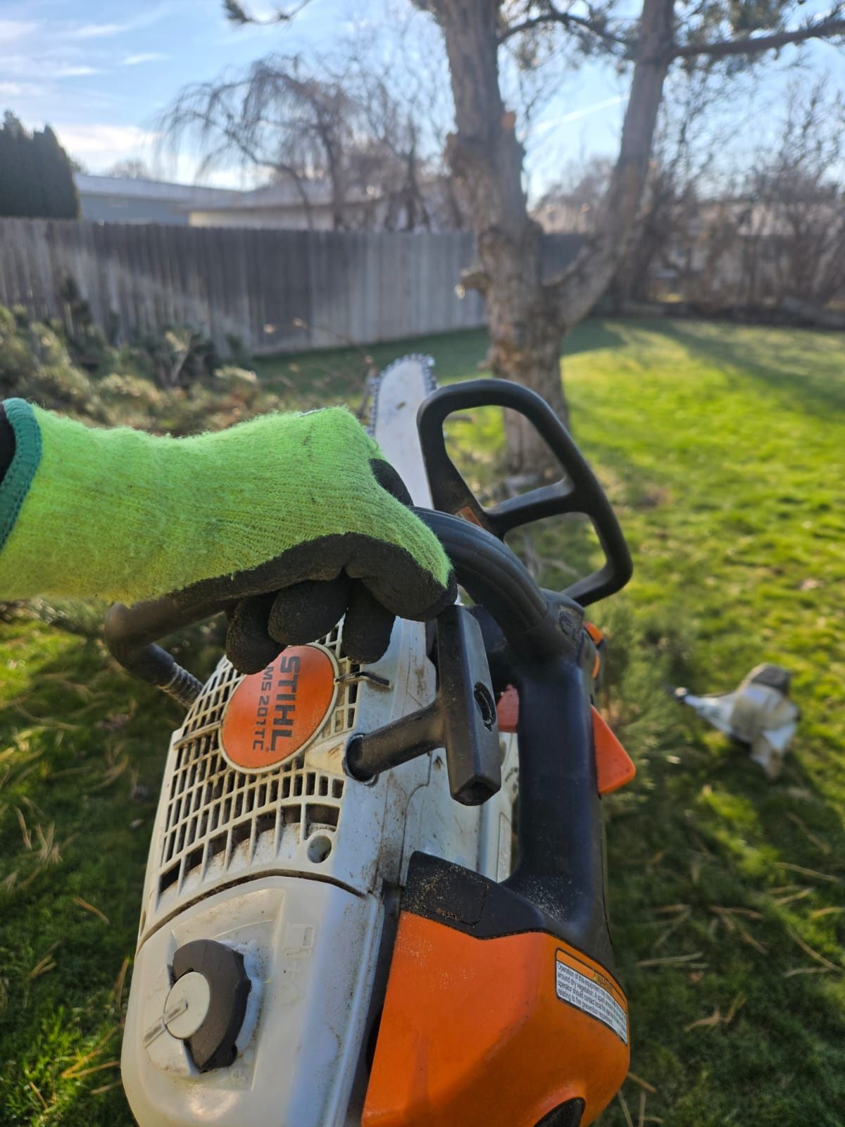 A person is holding a chainsaw in a yard.