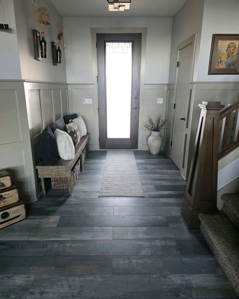 Narrow hallway with gray wood floors, a rug runner, bench, decor, and a bright door at the end