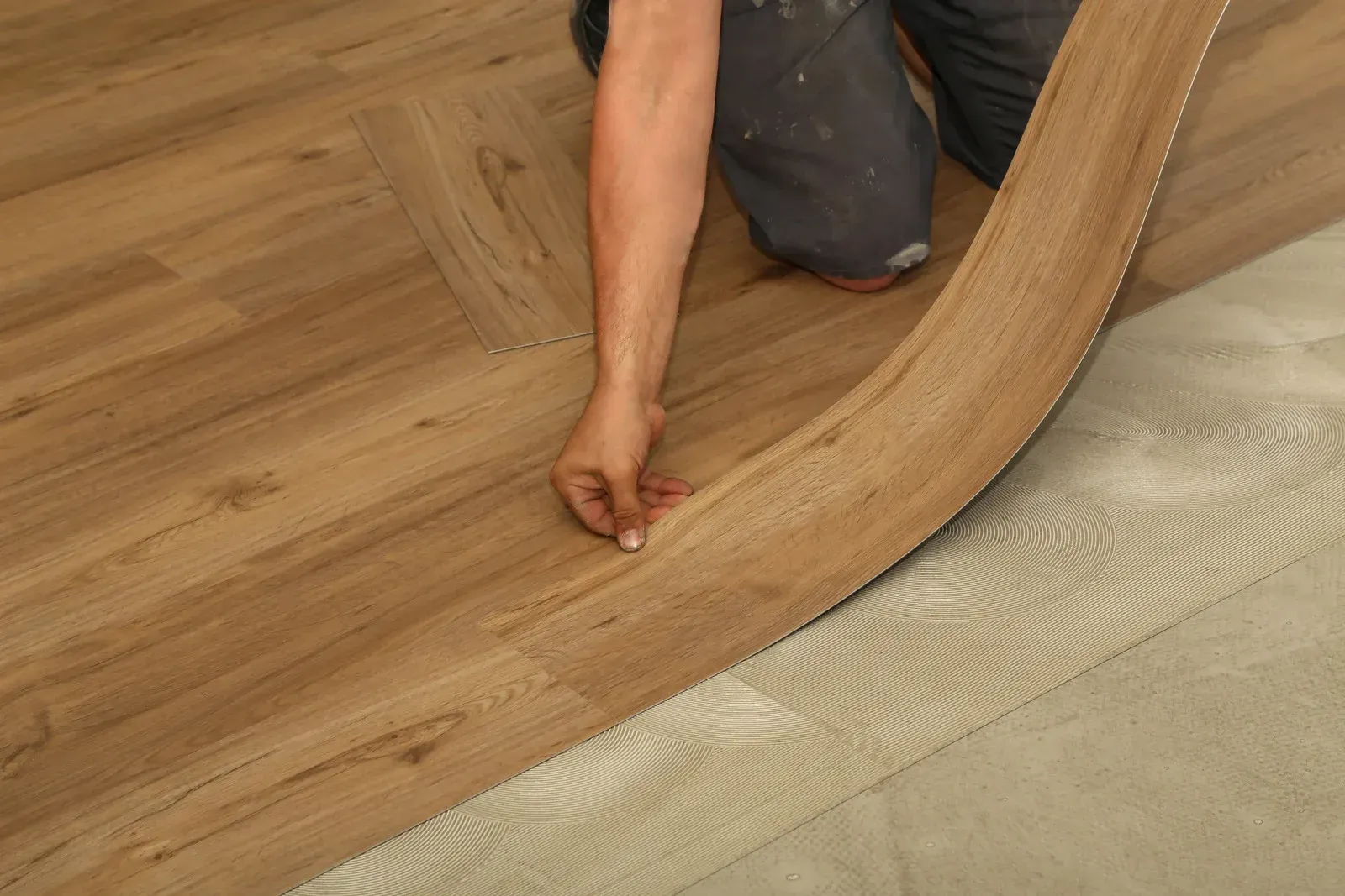 Installer laying a wood floor plank over underlayment in a room under construction