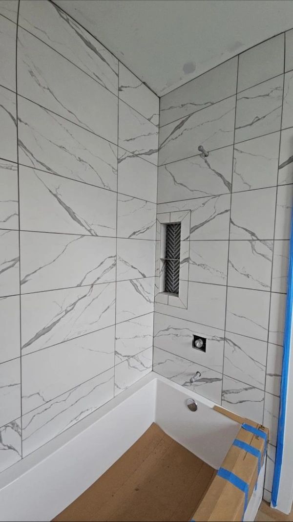 Tiled shower alcove with recessed niche, drain, and unfinished floor protection under construction