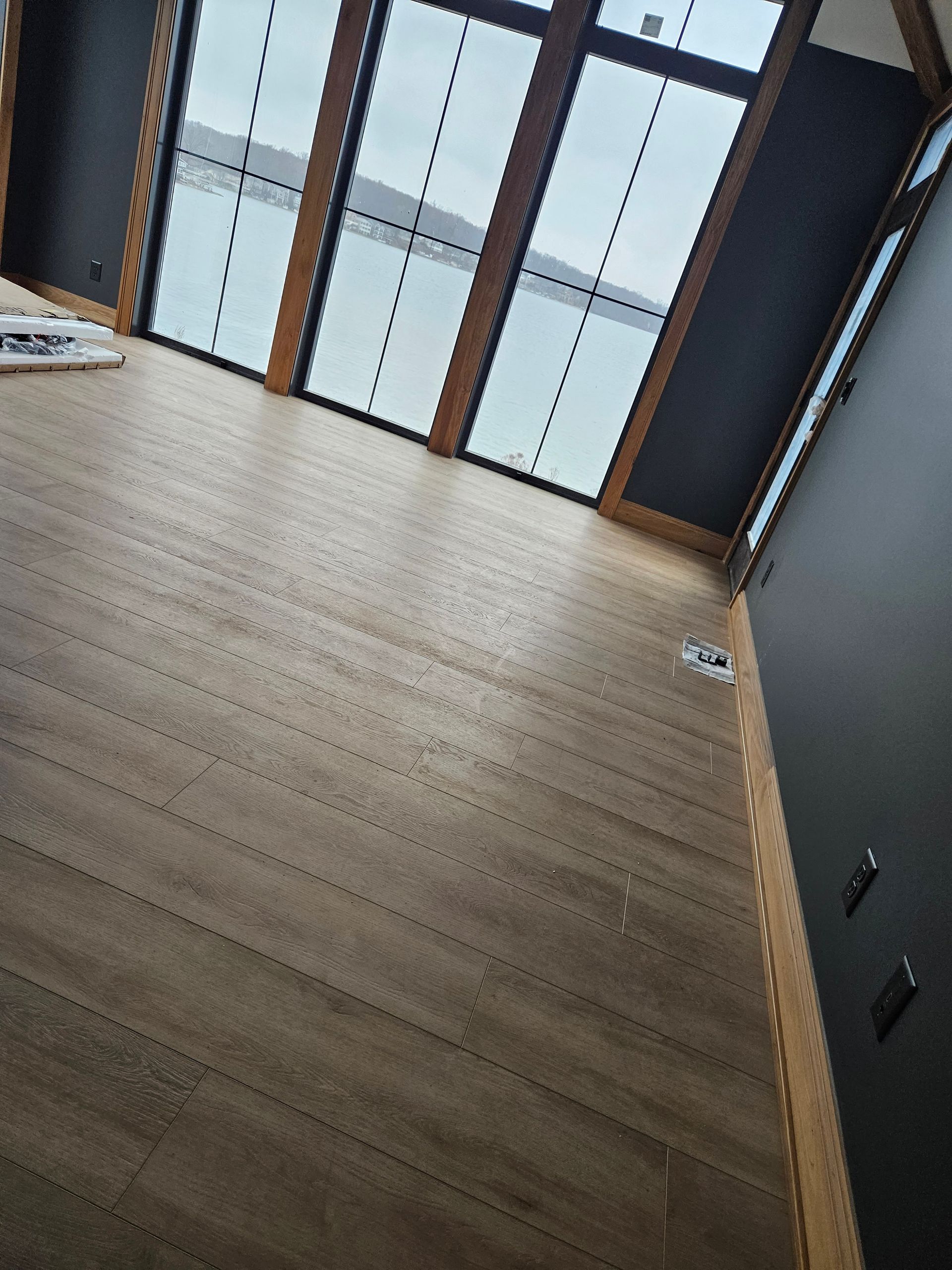 Empty room with light wood floor, dark gray walls, and large windows at the far end.