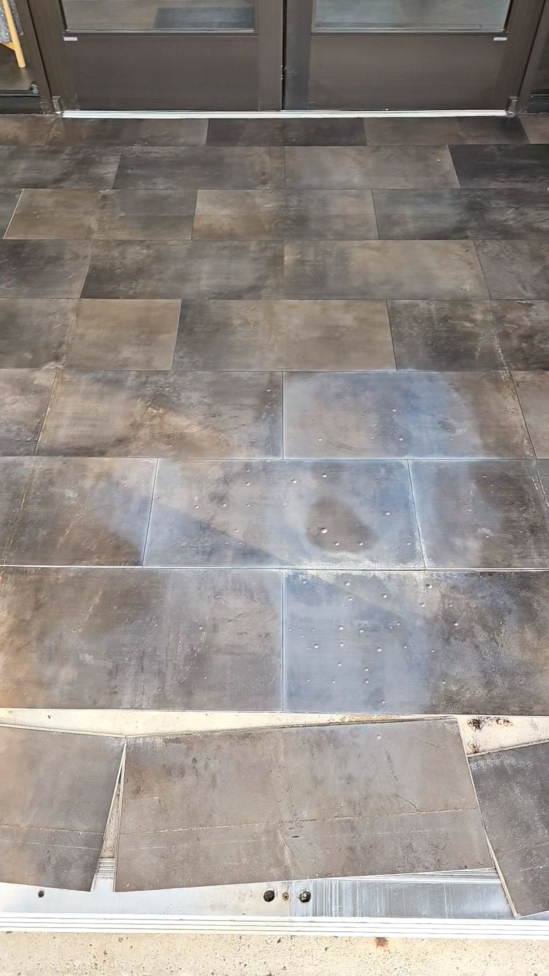 Tiled entryway with dark gray floor tiles leading to a glass door threshold
