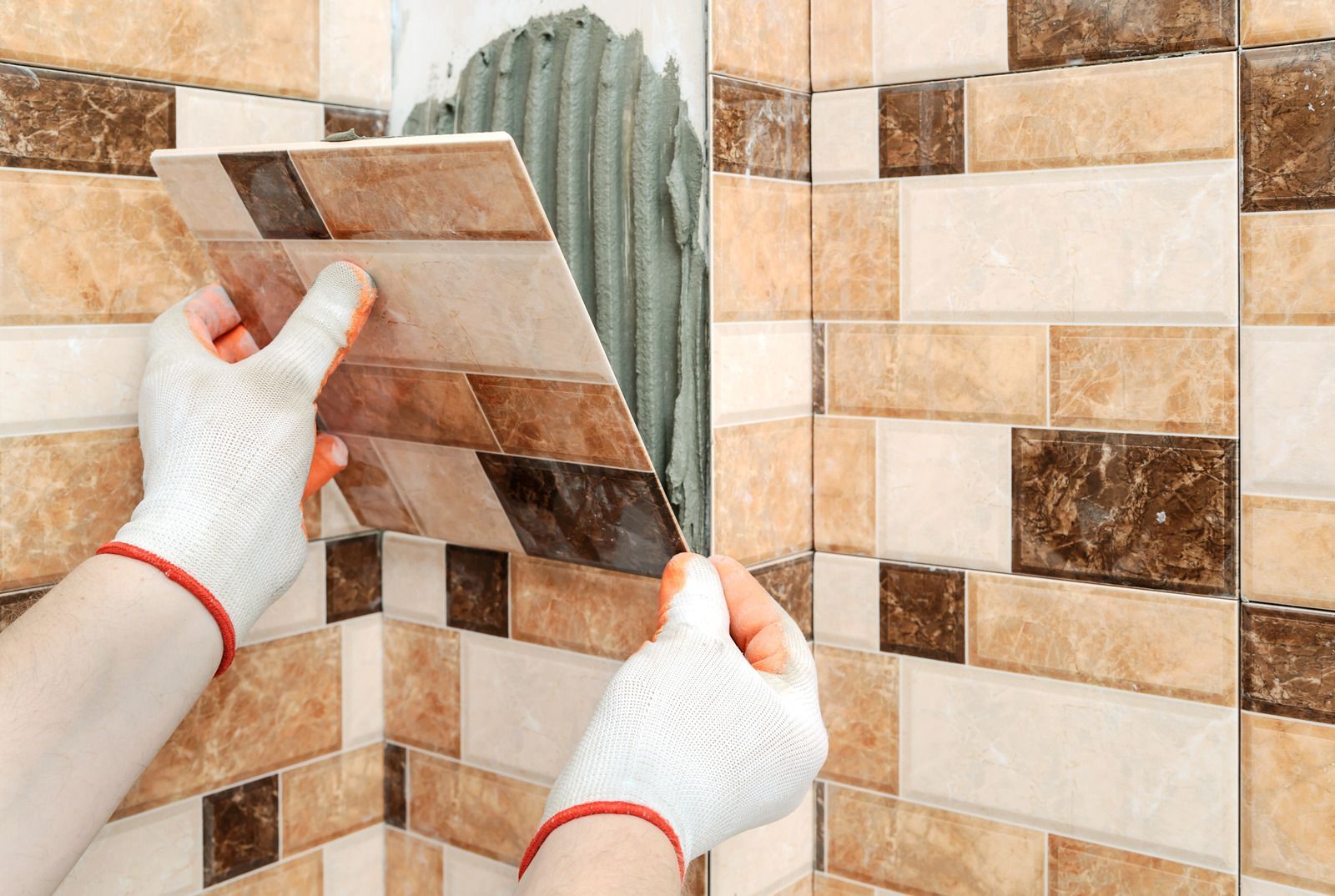 Hands tiling a beige and brown patterned wall with a replacement tile piece