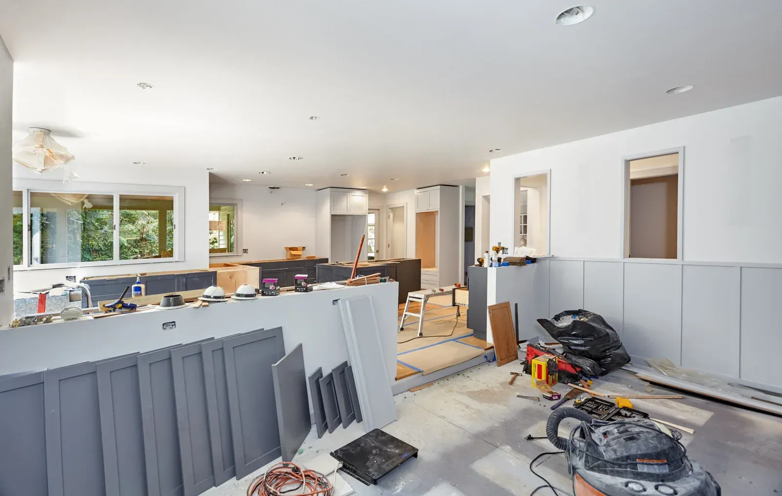 Construction zone in a bright kitchen and living area, with cabinets, tools, and materials scattered around.