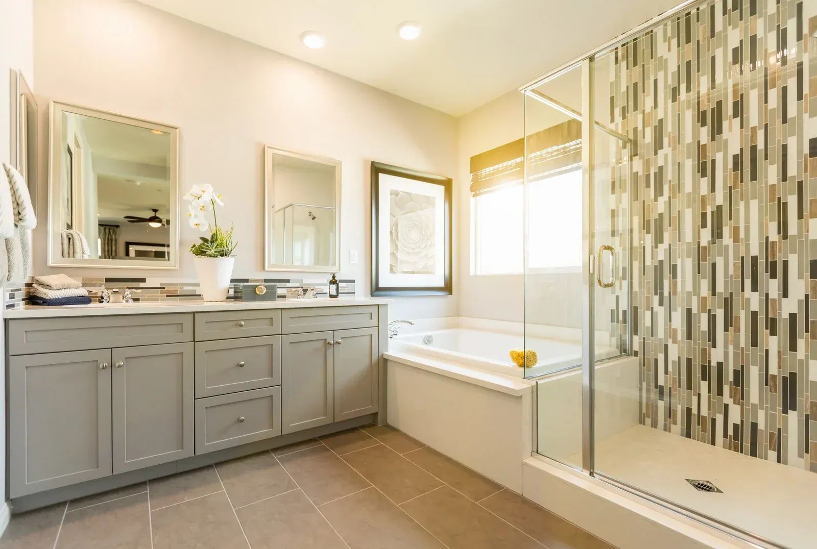 Bright bathroom with double vanity, mirrors, bathtub, and glass walk-in shower with patterned tile.