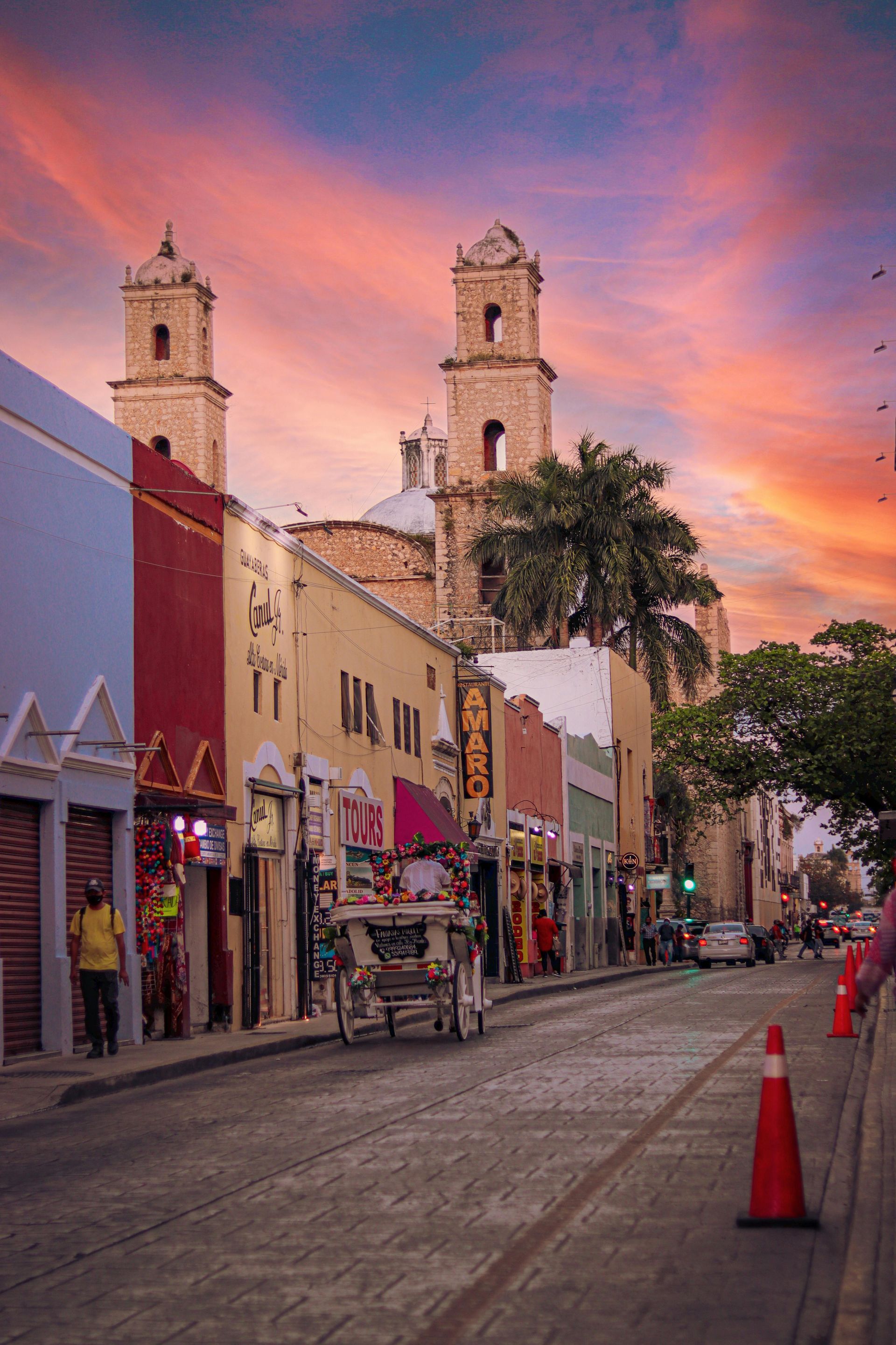 Holidays to Mexico - A horse drawn carriage is driving down a city street at sunset. Merida