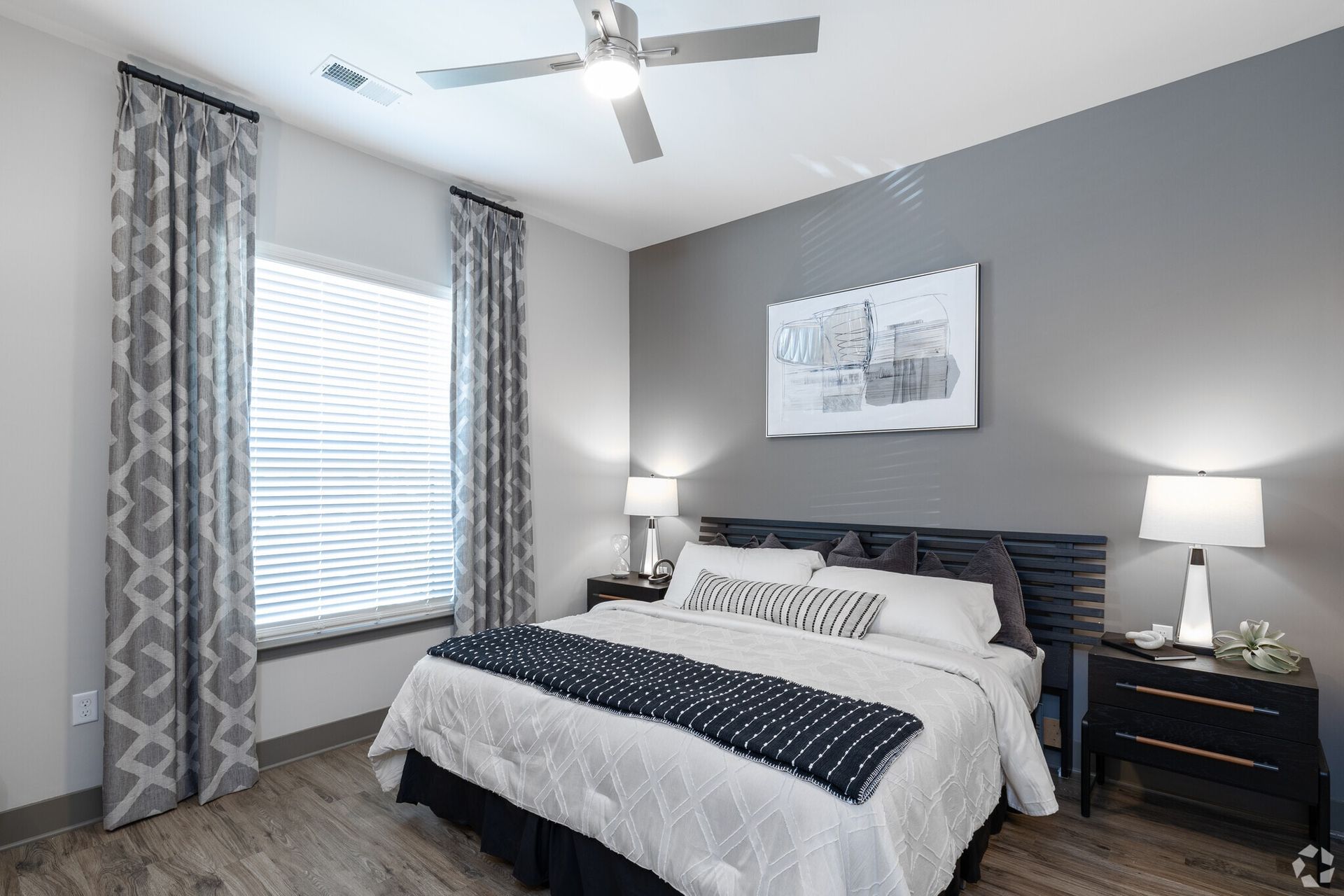 Bedroom in a modern apartment with a queen bed, nightstands, lamps, and a gray accent wall. Explore your next chapter with thoughtfully designed apartments in Louisville, KY—come see what life at The Terra feels like.
