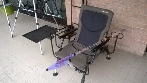 Una sedia da pesca con attaccato un ombrello viola.