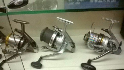 Tre mulinelli da pesca sono allineati su uno scaffale di vetro