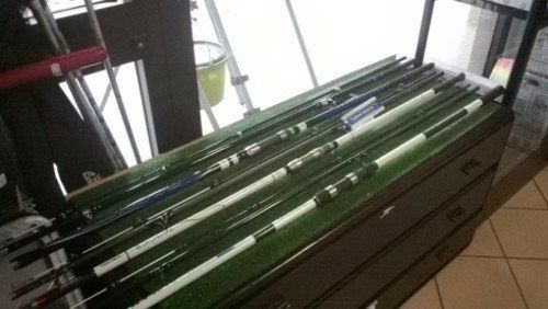 Un mucchio di canne da pesca sono appoggiate su uno scaffale in un negozio.