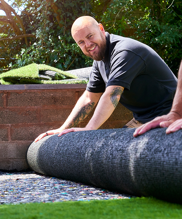 A man is laying a roll of artificial grass on the ground.