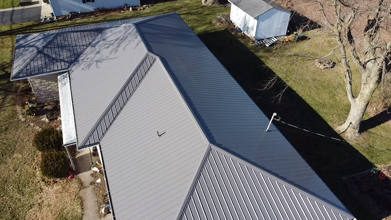 Overhead view of a house with a multi-paneled, dark metal roof. Tan and dark gray panels are visible.