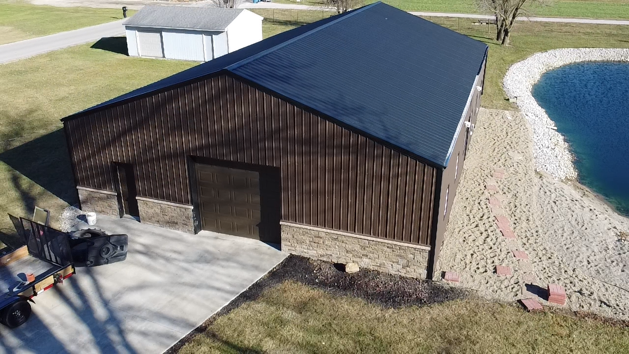 Brown and stone building with dark roof, next to a pond and concrete driveway.