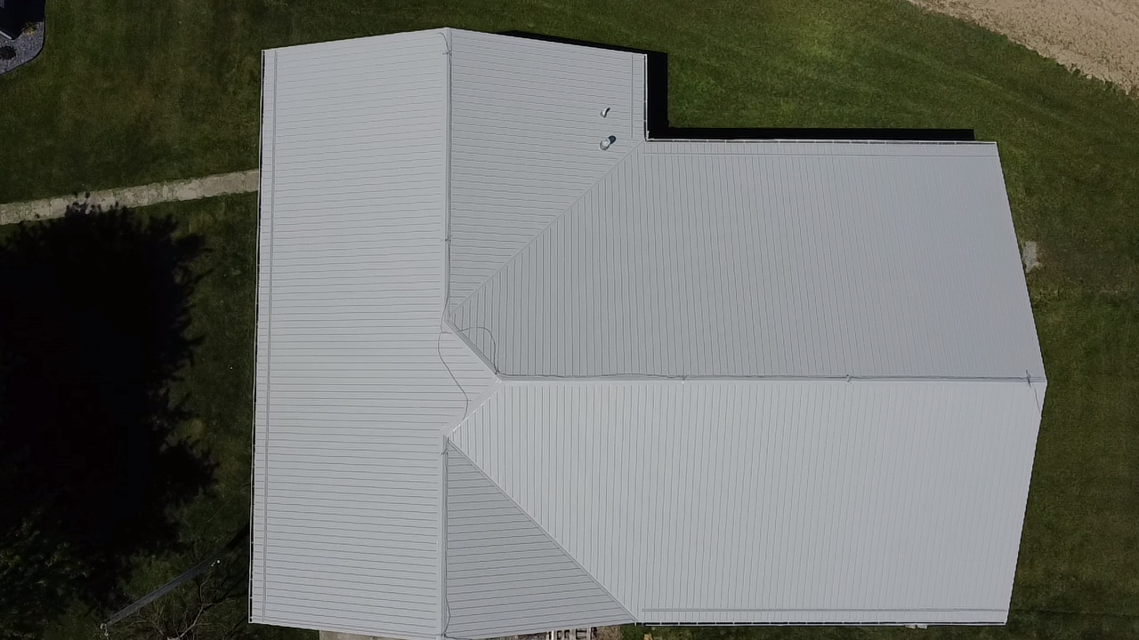 Overhead view of a metal building with a light-colored roof and surrounding green grass.