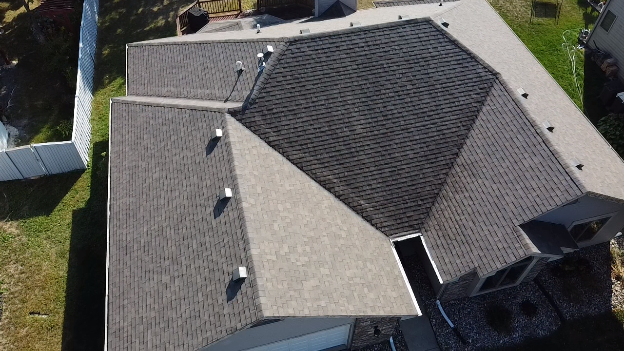 Overhead view of a dark gray asphalt shingle roof on a house with several angles and a chimney.