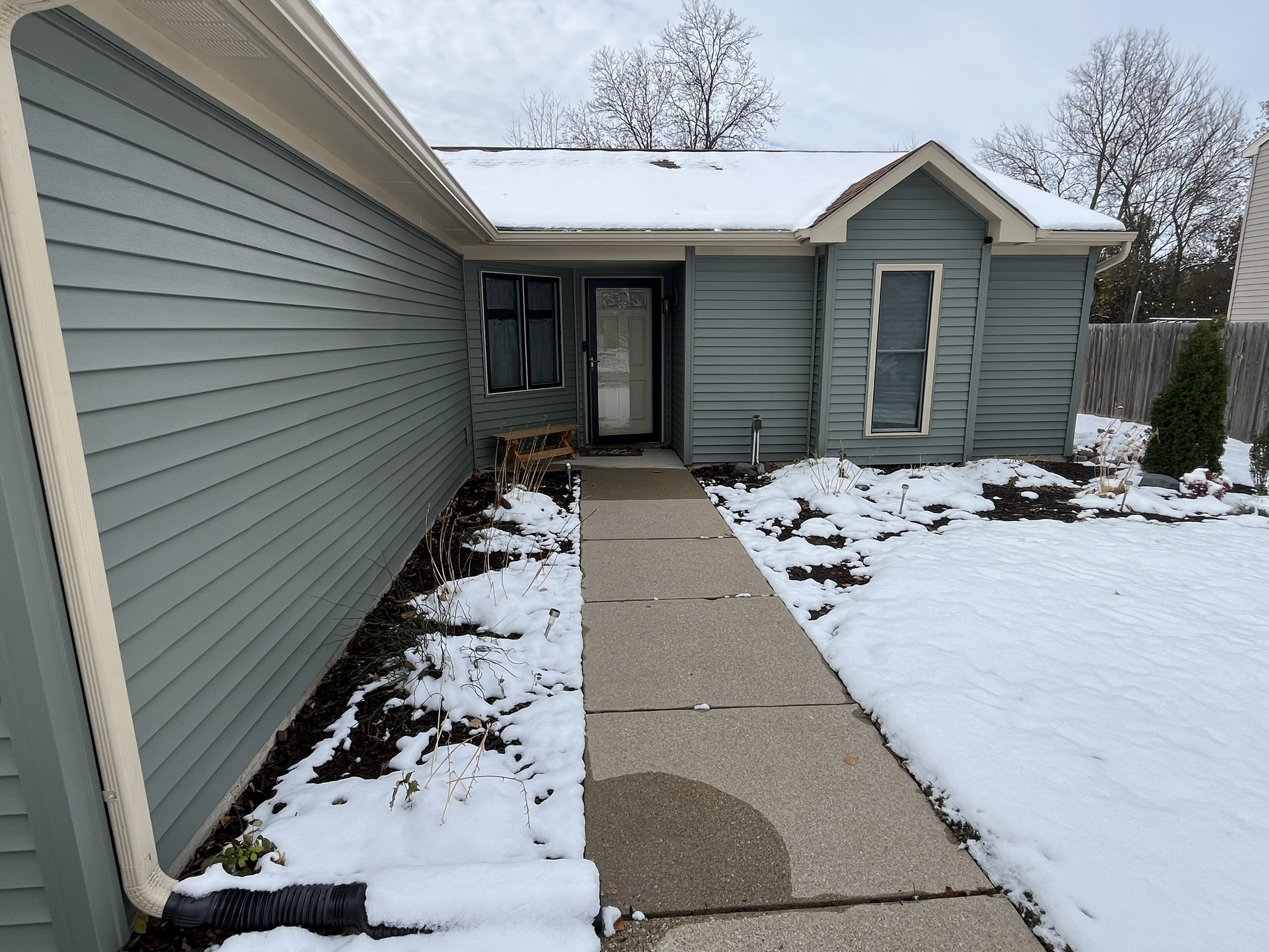 Snowy house exterior, blue siding, concrete walkway, snow-covered landscaping, cloudy sky.