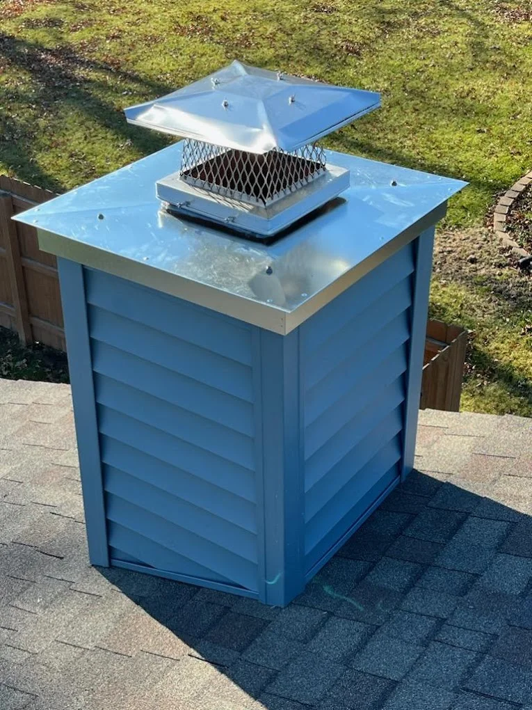 Blue-sided chimney on a roof with a metal top and chimney cap.