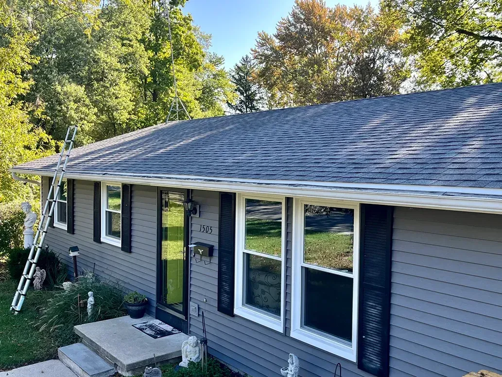 Gray house with new roof, white trim, black shutters, and ladder.
