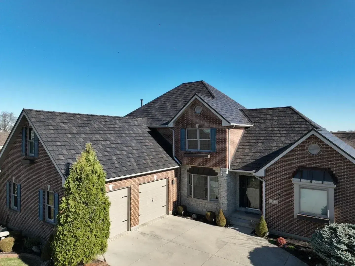House with brick facade and dark roof under a clear blue sky.