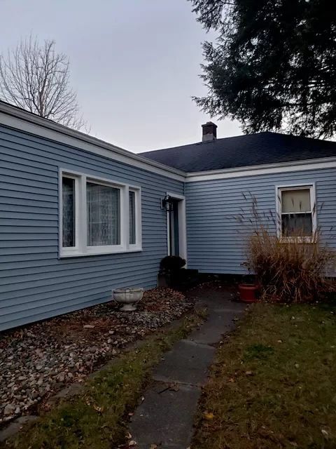 Light blue house with white trim, dark roof, and a concrete walkway. Overcast day.