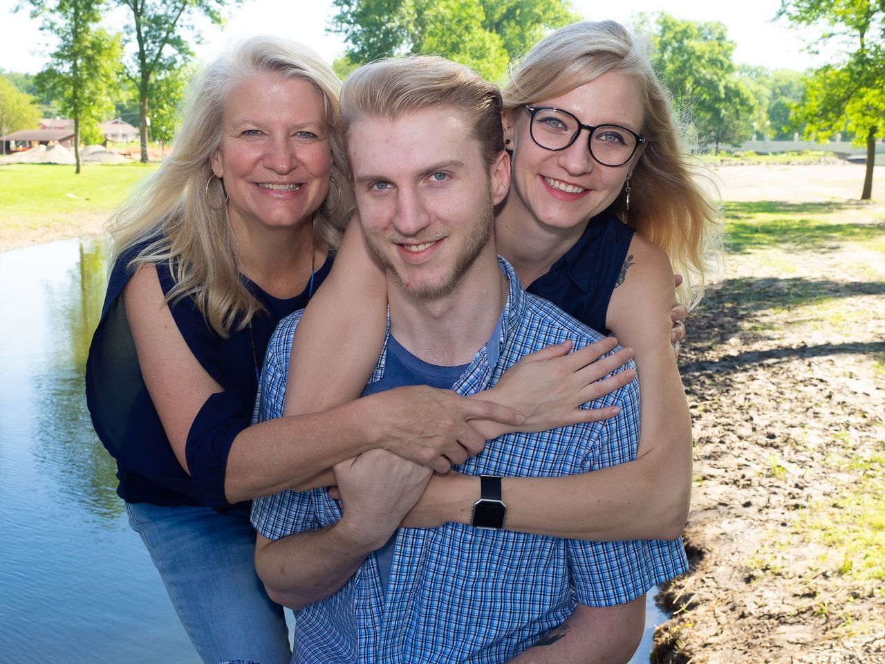 A woman and two girls are hugging a man in a park.