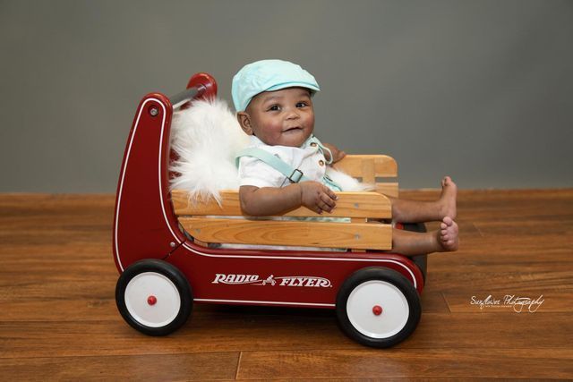 A baby is sitting in a red radio flyer wagon.