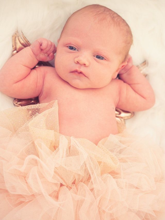A newborn baby is wearing a pink tutu and laying on a bed.