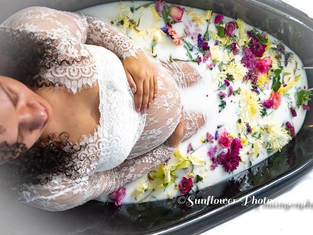 A pregnant woman is laying in a bathtub filled with milk and flowers