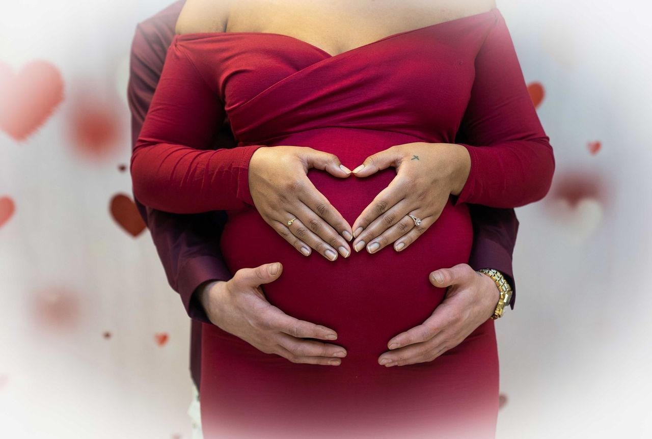 A pregnant woman is making a heart shape with her hands on her belly.