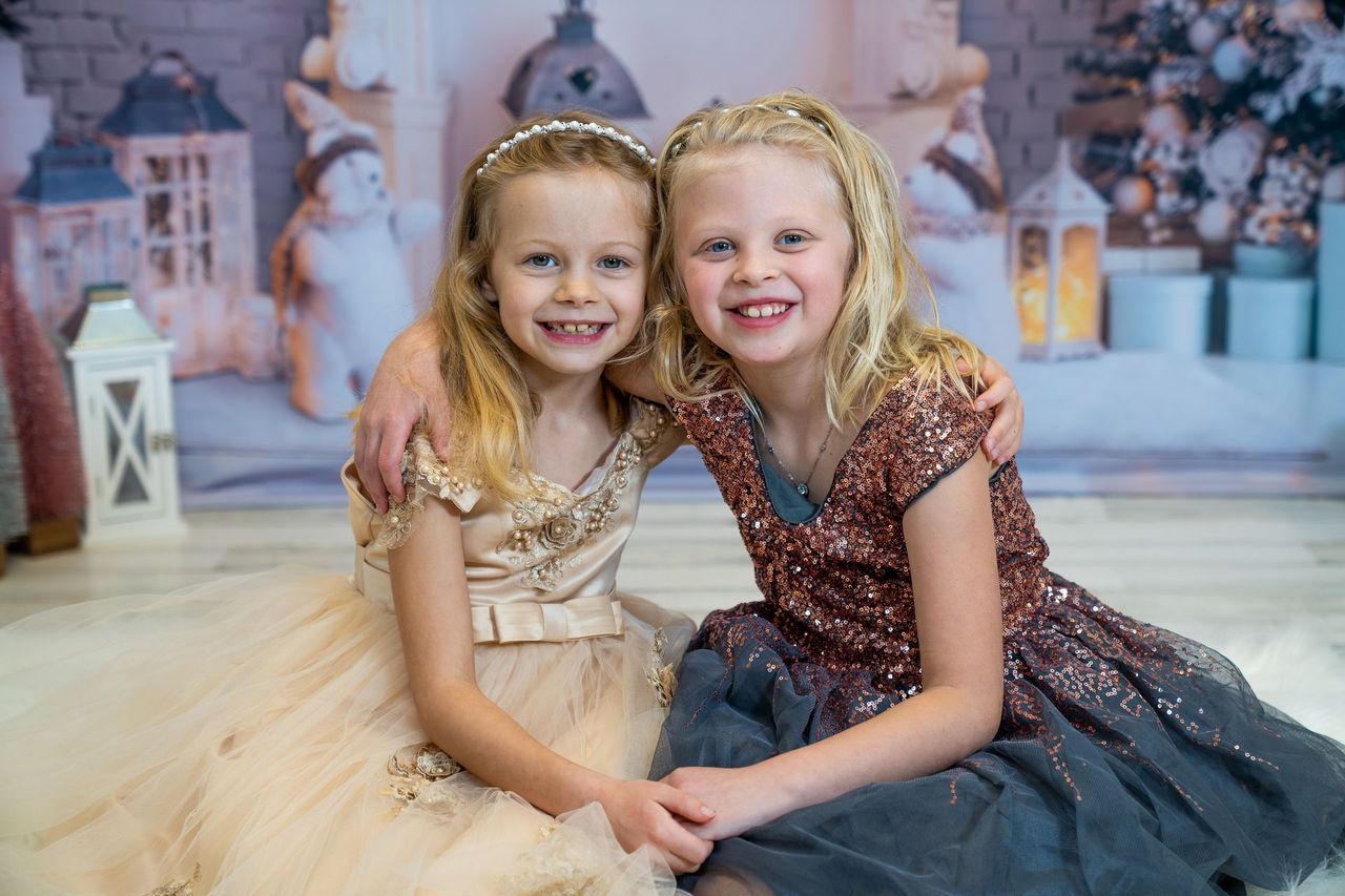 Two little girls in dresses are sitting next to each other on the floor.