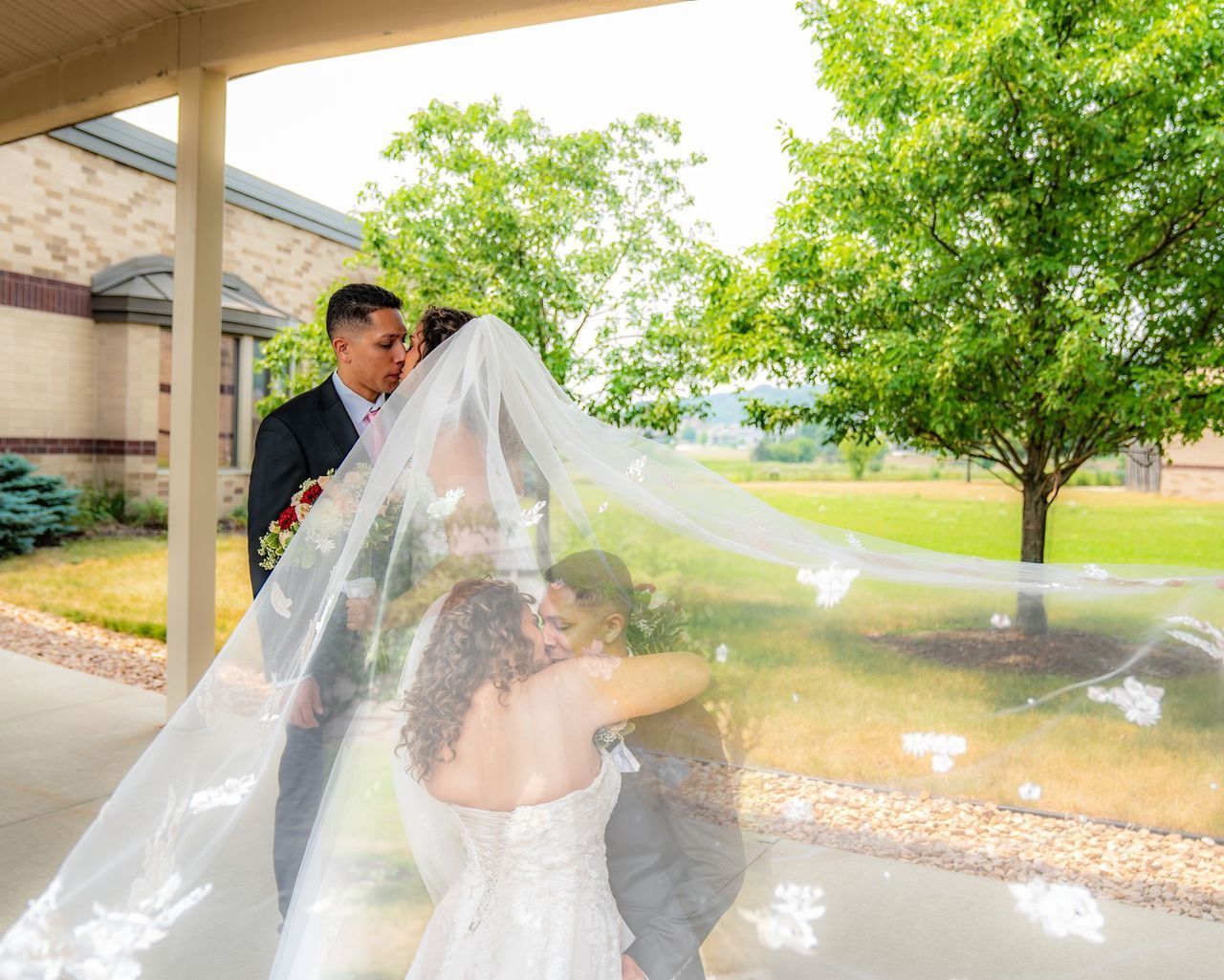 A bride and groom are posing for a picture with their veil blowing in the wind.