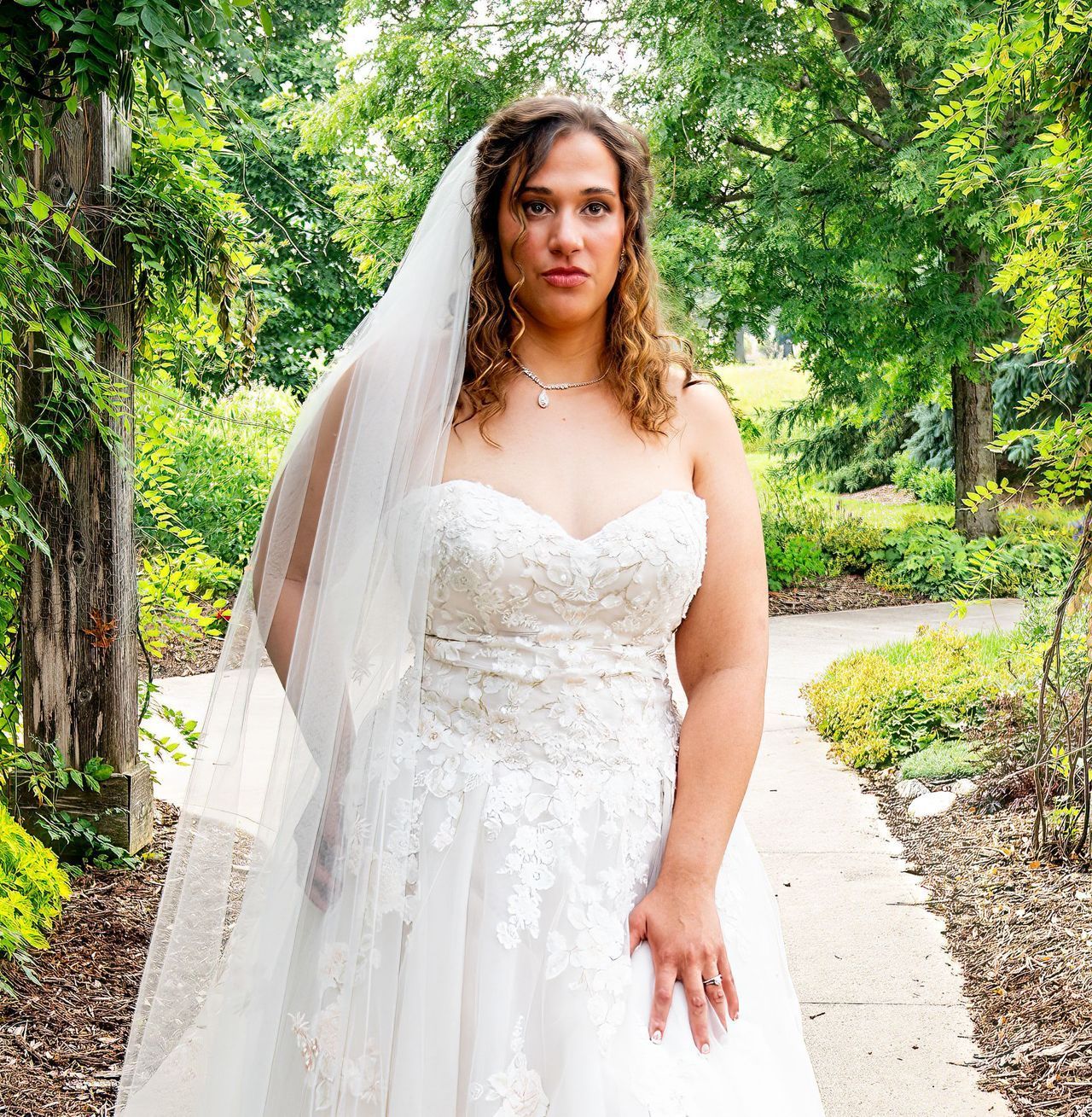 A woman in a wedding dress and veil is standing on a sidewalk.