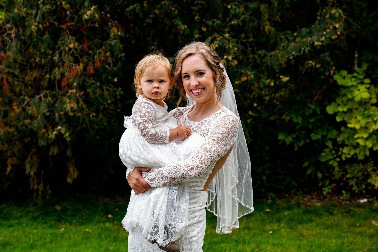 A bride is holding a flower girl in her arms.