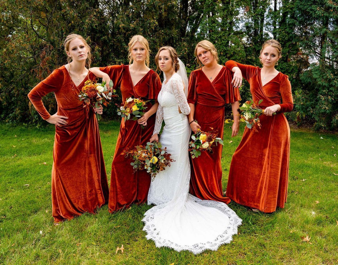 A bride and her bridesmaids are posing for a picture in the grass.