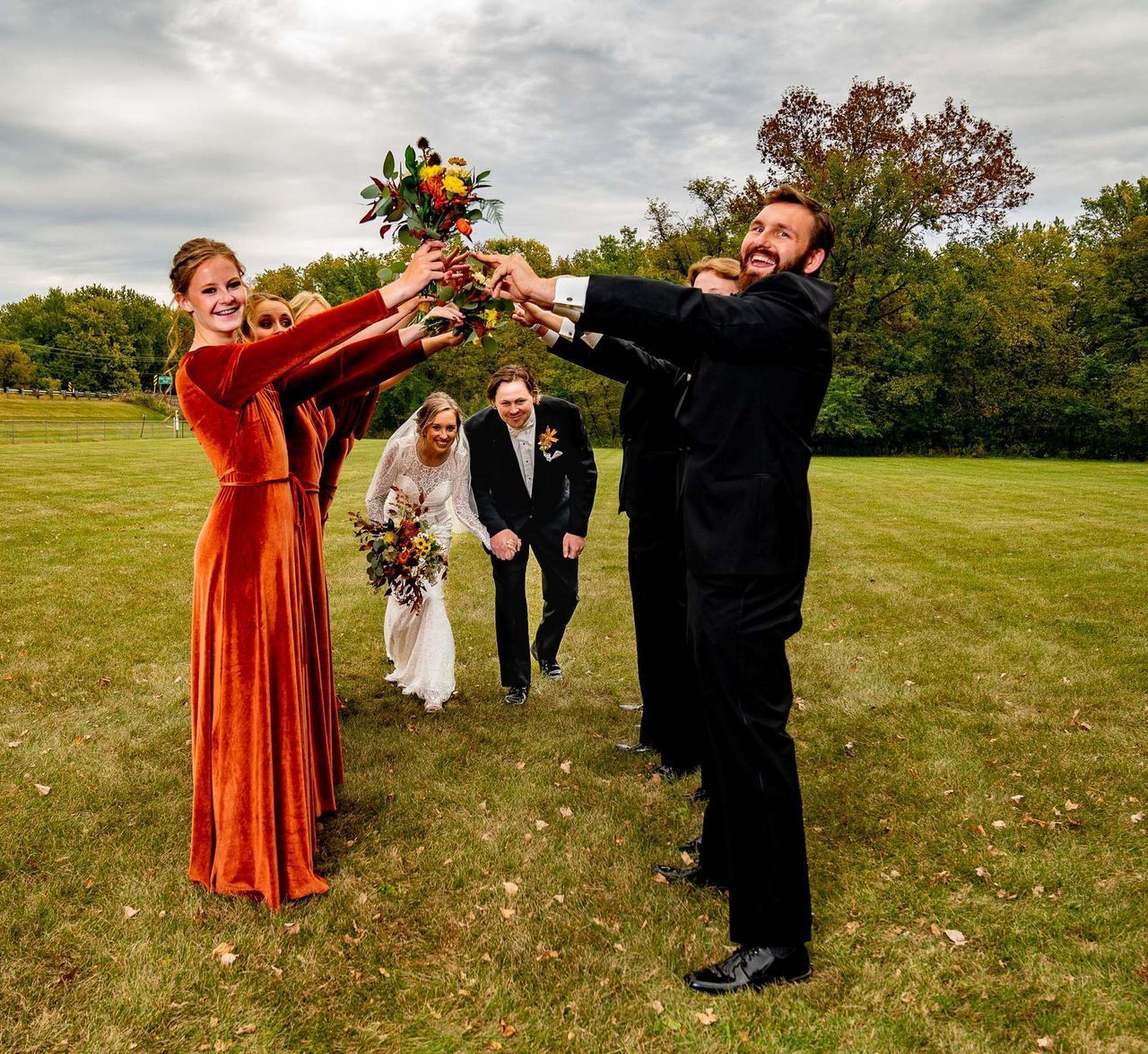A bride and groom are toasting with their wedding party in a field.
