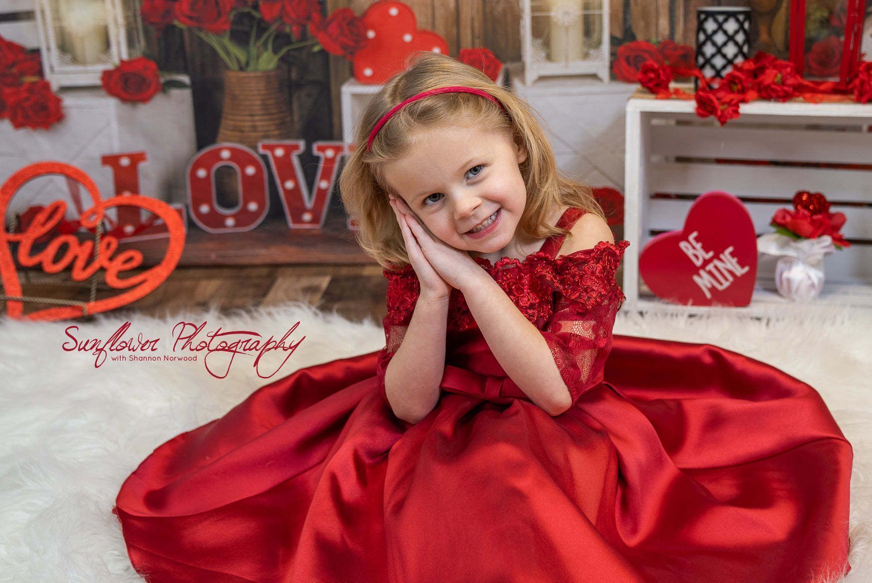 A little girl in a red dress is sitting on the floor.