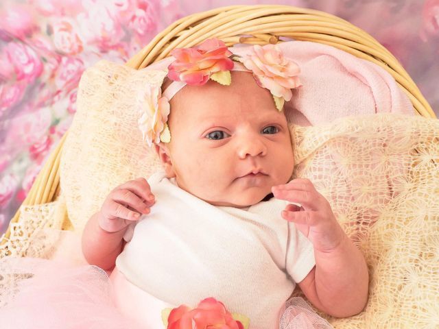 A newborn baby is laying in a wicker basket with a flower headband.