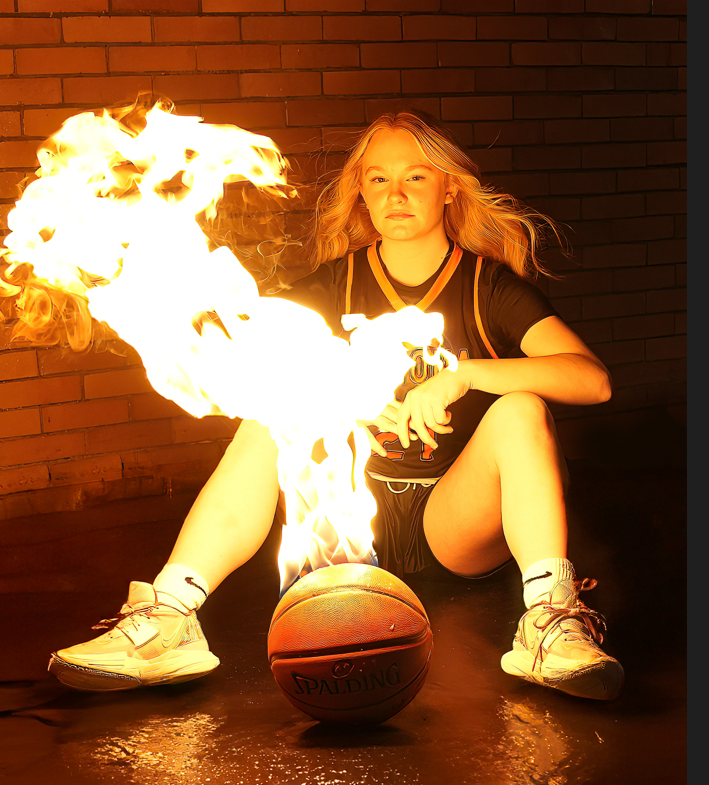 A girl is sitting next to a basketball with flames coming out of it