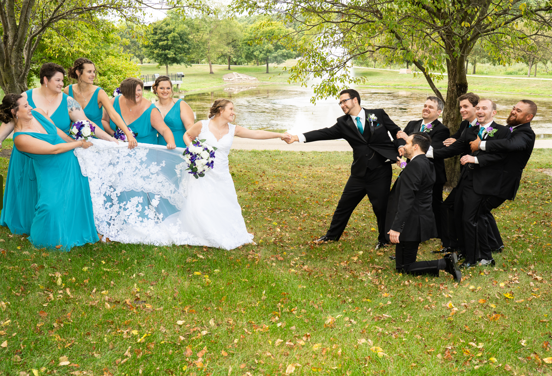 A bride and groom are holding hands with their wedding party in a park.