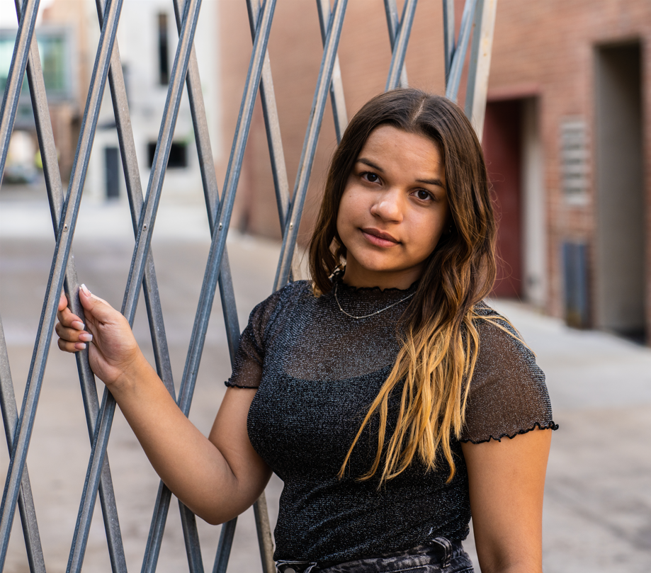 A woman in a black top is leaning against a metal fence