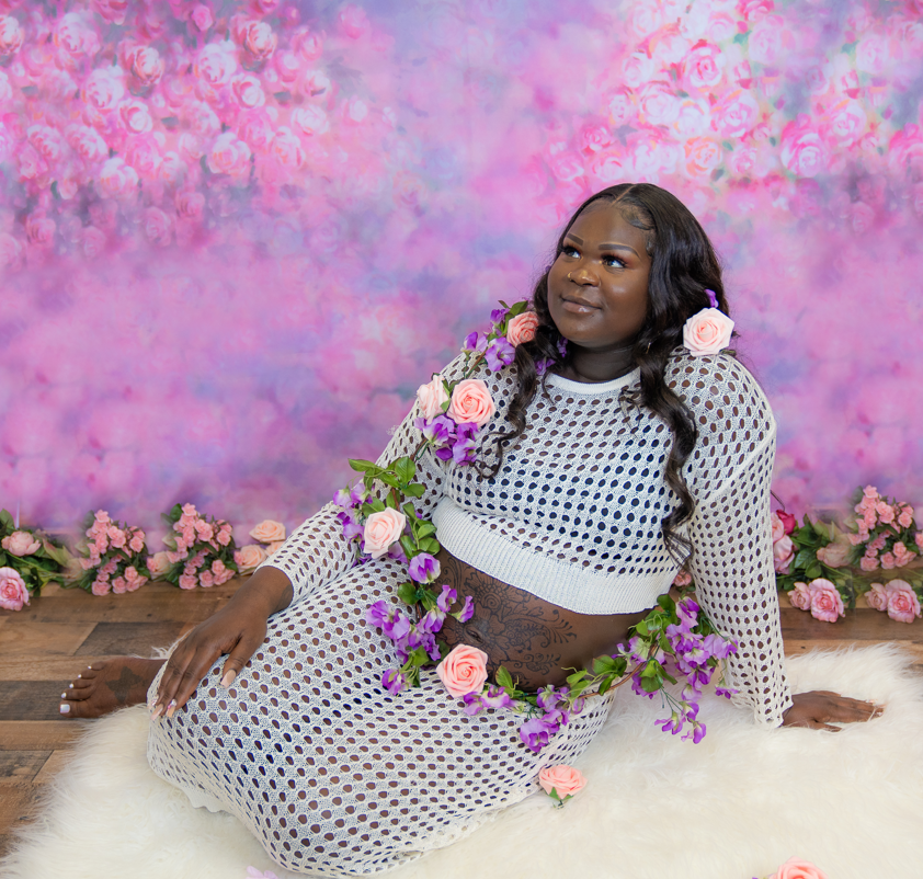 A pregnant woman is sitting on the floor with flowers around her belly.